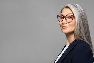 elegant asian businesswoman with grey hair in eyeglasses isolated on grey