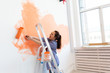 © satura_ - Renovation, redecoration and repair concept - Cheerful woman painting wall in new home.