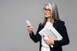 © LIGHTFIELD STUDIOS - confident asian businesswoman in eyeglasses using smartphone and holding business newspaper isolated on grey