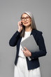 © LIGHTFIELD STUDIOS - attractive asian businesswoman with grey hair talking on smartphone and holding laptop isolated on grey
