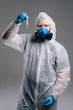 © dikushin - Scientist in protective suit, goggles and respirator is holding test tube in hand. Concept of working on coronavirus vaccine. Studio shot on dark background.