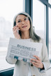 © LIGHTFIELD STUDIOS - confident asian businesswoman in eyeglasses talking on smartphone and holding business newspaper in office