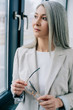 © LIGHTFIELD STUDIOS - beautiful asian businesswoman with grey hair in grey suit holding eyeglasses and looking through window