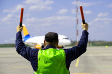 An Airport Marshal In A Yellow Uniform Will Help Signals To Park By Plane. The Supervisor Meets A Passenger Plane At The Airport. The Plane Steers Into The Parking Lot.