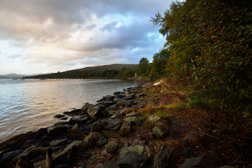 Rocky lake shores under the colorful evening sky after the rain. Dramatic cloudscape. Gare Loch, Rhu, Scotland, UK