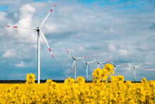 Windfarm In Northern Germany Surrounded By Yellow Raps Field And Blue Sky