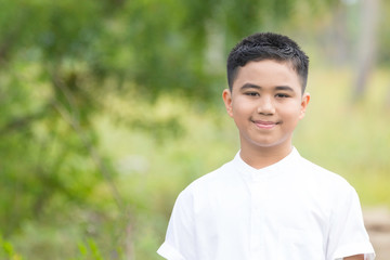 A portrait of a good looking Asian boy wearing a white shirt smiling in a park.