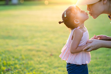 Mom and daughter kissing each other on the lips at park. Mother day concept