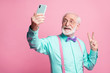 © deagreez - Portrait of positive cheerful old man rest relax summer trip use smartphone take selfie make v-signs wear teal turquoise shirt purple violet bowtie isolated pastel pink color background