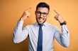 © Krakenimages.com - Young handsome businessman wearing tie and glasses standing over yellow background smiling pointing to head with both hands finger, great idea or thought, good memory