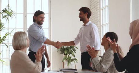 Canvas Print - Happy diverse multiracial older and younger colleagues watching male boss supervisor shaking hands, praising intern coworker in office. Smiling employees clapping hands, supporting successful worker.