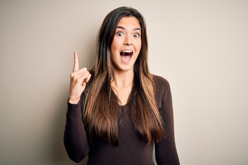 Poster - Young beautiful girl wearing casual sweater standing over isolated white background pointing finger up with successful idea. Exited and happy. Number one.