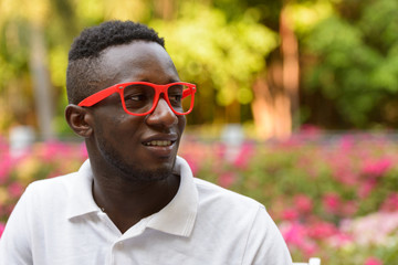 Wall Mural - Face of happy young African man with eyeglasses thinking at the park outdoors