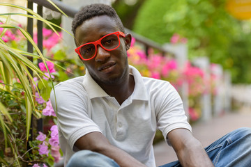 Wall Mural - Young African man with eyeglasses sitting at the park outdoors