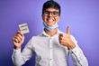 © Krakenimages.com - Young handsome man wearing medical mask holding reminder with corona virus message happy with big smile doing ok sign, thumb up with fingers, excellent sign