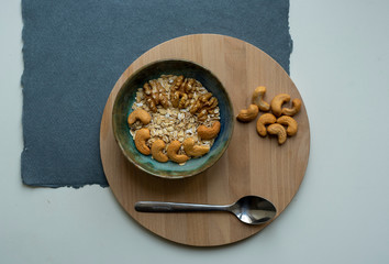 Oatmeal with cashews and walnuts on a wooden tray and blue and white background. Healthy breakfast