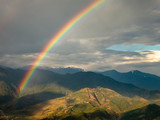 Fototapeta Tęcza - A beautiful, aerial view of a rainbow streaming through dark clouds over the green hills surrounding the village of Sarangkot near Pokhara in Nepal.