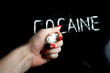 © Анастасия Гайкова - hand squeezes cellophane bag with white powder (drug), the word 'cocaine' on a black background