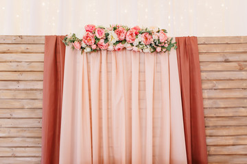 Rustic wedding photo zone. Wedding in the style vintage. Composition with flowers on a wooden stand. A wooden backdrop of chiffon and flowers. Indoors wedding reception venue. Horizontal shot.