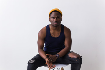 Wall Mural - Portrait of sexy trendy african man sitting on a chair on white background. Youth concept.