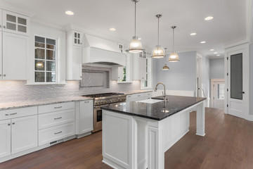Kitchen in new luxury home with large island, pendant lights, hardwood floor and stainless steel appliances.