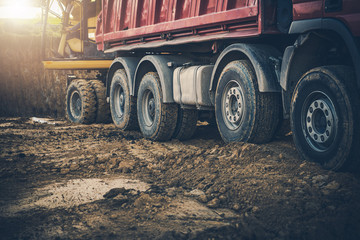 Construction Site With Worker Moving Soil From Backhoe To Dump Truck.