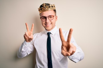 Wall Mural - Young handsome caucasian business man wearing golden crown over isolated background smiling looking to the camera showing fingers doing victory sign. Number two.