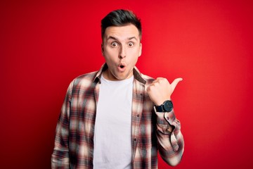 Young handsome caucasian man wearing casual modern shirt over red isolated background Surprised pointing with hand finger to the side, open mouth amazed expression.