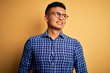 © Krakenimages.com - Young handsome latin man wearing casual shirt and glasses over yellow background looking away to side with smile on face, natural expression. Laughing confident.