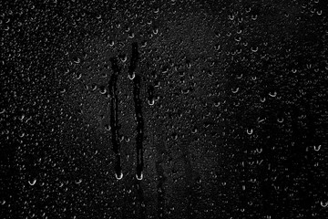 Drops of water flow down the surface of the clear glass on a black background.	
