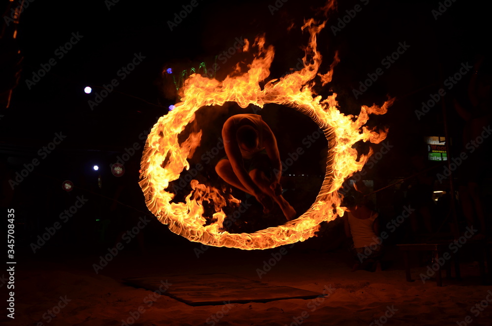 Mężczyzna skaczący przez ognisty krąg  podczas full moon party na wyspie Phi Phi w Tajlandii - obrazy, fototapety, plakaty 
