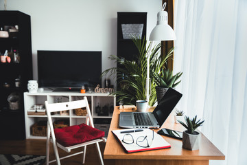 Welcome to my home office - shot of technology and a notebook on a desk in an empty home office during the day. Work from home concept with laptop, phone, notebook and pen left on the work table