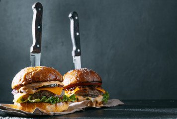 Canvas Print - Two mouth-watering, delicious homemade burger used to chop beef. on the wooden table. The burgers are inserted knives.