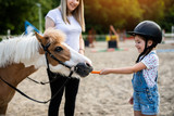 Cute little girl and her older sister enjoying with pony horse outdoors at ranch.