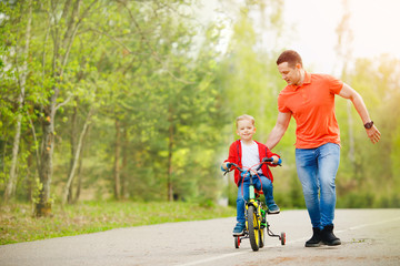 Happy father teaching his little son to ride bicycle. Child learning bike with dad