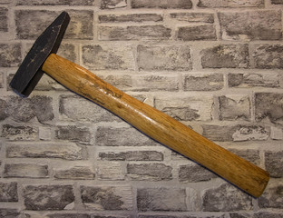 Black metal hammer with wooden handle on a brick wall background.