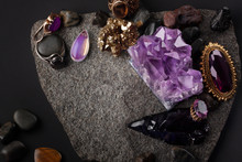 Stone Background With A Scattering Of Old Jewelry, Rings, Brooches, Amethyst Druse, Obsidian, Moonstone, Gold. Dark Layout For Beauty Design In Violet And Gold Colors. 