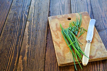 Wall Mural - First greens, chives and knife on a wooden board on a wooden background.