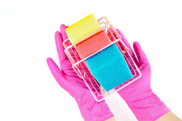 Female hands wearing pink disposable gloves hold a small shopping basket full of multicolored dish washing sponges. Top view, isolated on white.