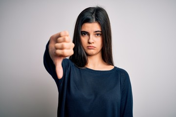 Wall Mural - Young beautiful brunette woman wearing casual sweater standing over white background looking unhappy and angry showing rejection and negative with thumbs down gesture. Bad expression.