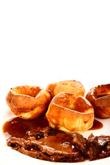 Traditional british meal of roast beef and yorkshire puddings with gravy on a white plate