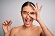 © Krakenimages.com - Young beautiful brunette woman holding dental aligner orthodontic to teeth corretion with happy face smiling doing ok sign with hand on eye looking through fingers
