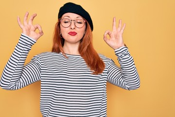 Canvas Print - Beautiful redhead woman wearing striped t-shirt and french beret over yellow background relax and smiling with eyes closed doing meditation gesture with fingers. Yoga concept.