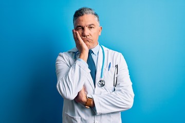 Poster - Middle age handsome grey-haired doctor man wearing coat and blue stethoscope thinking looking tired and bored with depression problems with crossed arms.