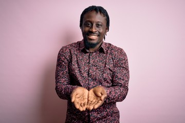 Sticker - Young handsome african american man wearing casual shirt standing over pink background Smiling with hands palms together receiving or giving gesture. Hold and protection