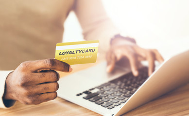 African American customer with loyalty card and laptop shopping via internet indoors, closeup
