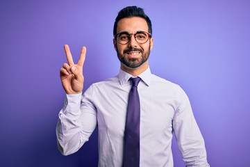 Sticker - Handsome businessman with beard wearing casual tie and glasses over purple background smiling with happy face winking at the camera doing victory sign. Number two.