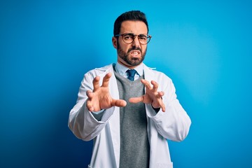 Sticker - Young handsome doctor man with beard wearing coat and glasses over blue background disgusted expression, displeased and fearful doing disgust face because aversion reaction. With hands raised