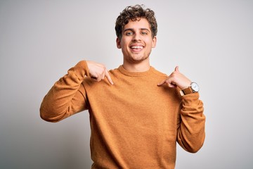 Young blond handsome man with curly hair wearing casual sweater over white background looking confident with smile on face, pointing oneself with fingers proud and happy.