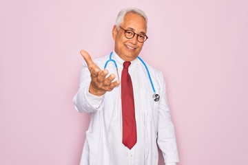 Canvas Print - Middle age senior grey-haired doctor man wearing stethoscope and professional medical coat smiling cheerful offering palm hand giving assistance and acceptance.